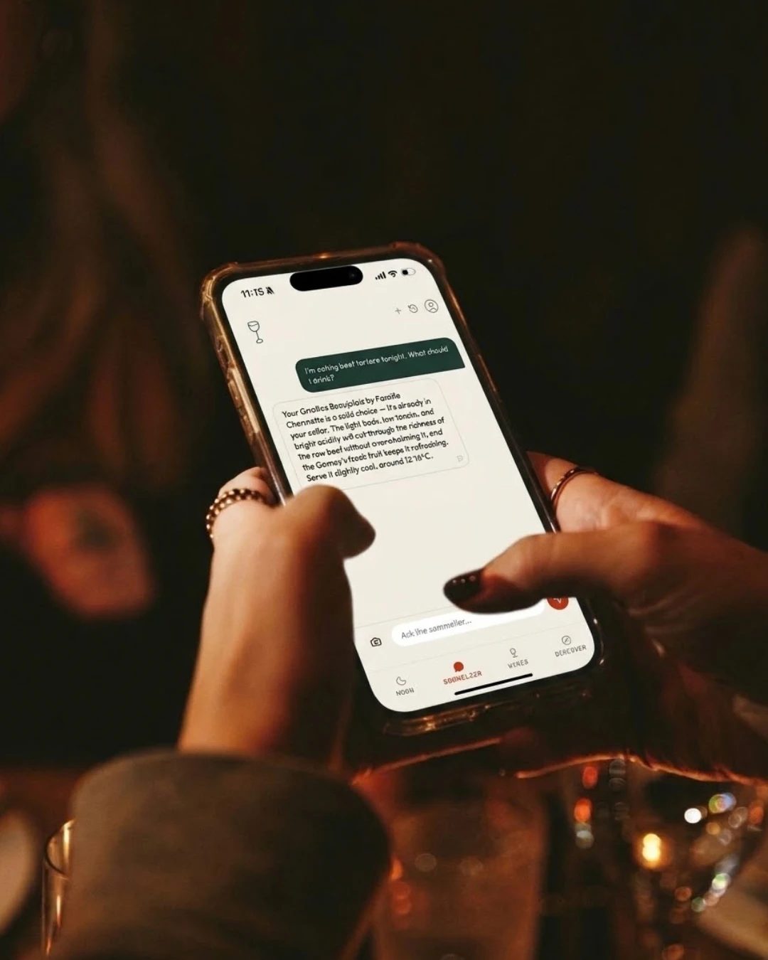 Deux mains tenant un téléphone qui affiche la caviste de Thirsty Cellar, à une table éclairée à la chandelle