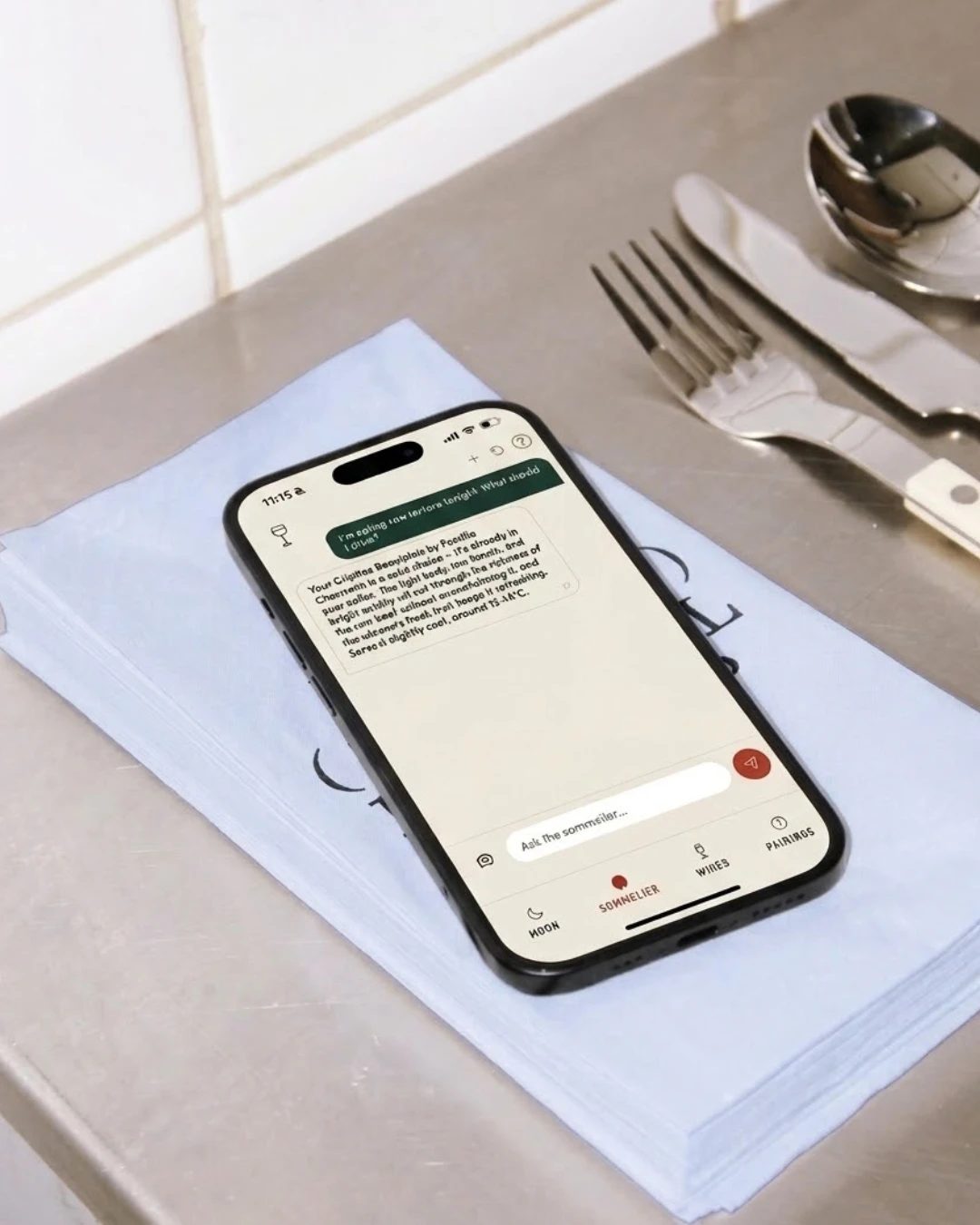 Un téléphone sur une serviette pliée, à côté des ustensiles, sur un comptoir d’acier