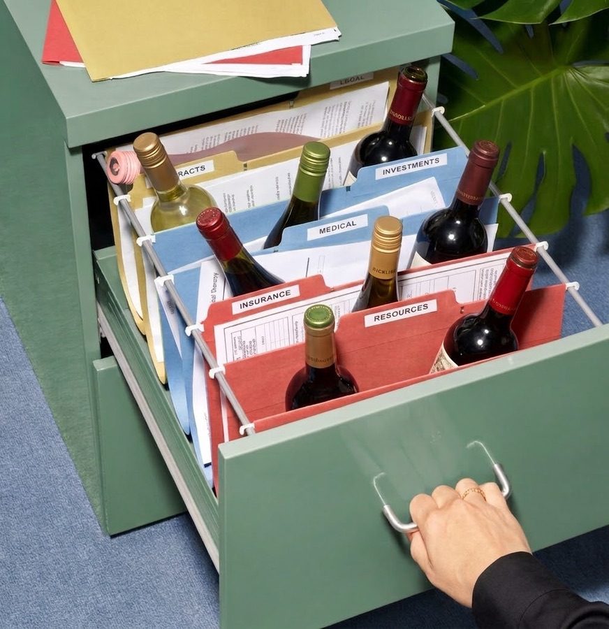 Wine bottles filed in a green filing-cabinet drawer between folders labelled Insurance, Medical and Investments