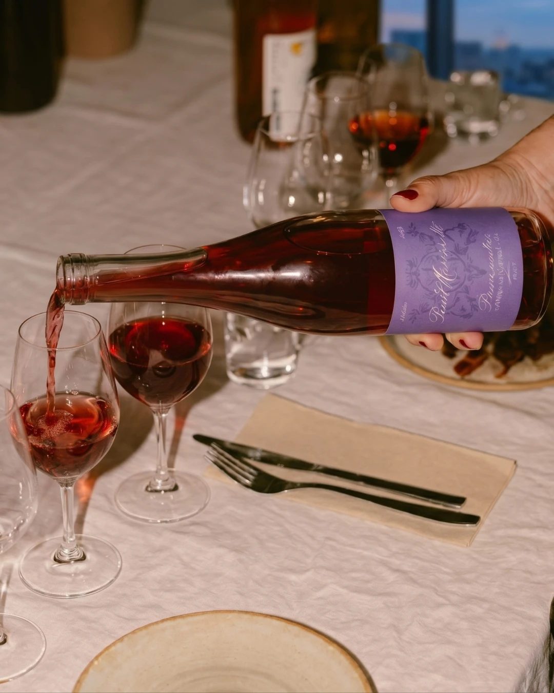 Du vin rouge versé dans des verres sur une table dressée, les ustensiles posés sur une serviette de lin