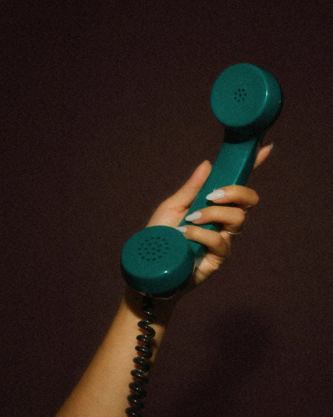 Une main tenant un combiné de téléphone turquoise contre un mur brun foncé